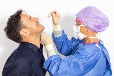 Koruyucu kıyafetli bir doktor olası bir koronavirüs enfeksiyonu için kişinin burnundan örnek alıyor.