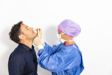 Koruyucu kıyafetli bir doktor olası bir koronavirüs enfeksiyonu için kişinin burnundan örnek alıyor.