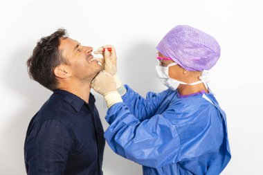 Koruyucu kıyafetli bir doktor olası bir koronavirüs enfeksiyonu için kişinin burnundan örnek alıyor.