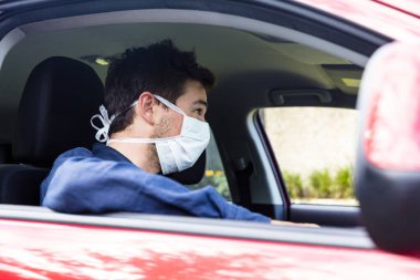 Arabanın içindeki koruyucu maskeli genç erkek sürücü.