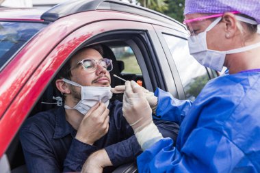 Koruyucu kıyafetli bir doktor olası bir koronavirüs enfeksiyonu için kişinin burnundan örnek alıyor.