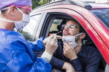 Koruyucu kıyafetli bir doktor olası bir koronavirüs enfeksiyonu için kişinin burnundan örnek alıyor.