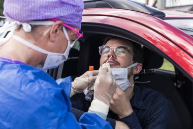 Koruyucu kıyafetli bir doktor olası bir koronavirüs enfeksiyonu için kişinin burnundan örnek alıyor.