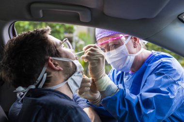 Koruyucu kıyafetli bir doktor olası bir koronavirüs enfeksiyonu için kişinin burnundan örnek alıyor.