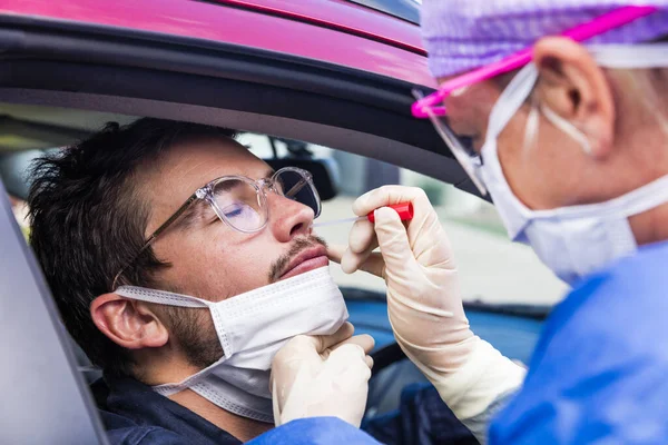 Koruyucu kıyafetli bir doktor olası bir koronavirüs enfeksiyonu için kişinin burnundan örnek alıyor.
