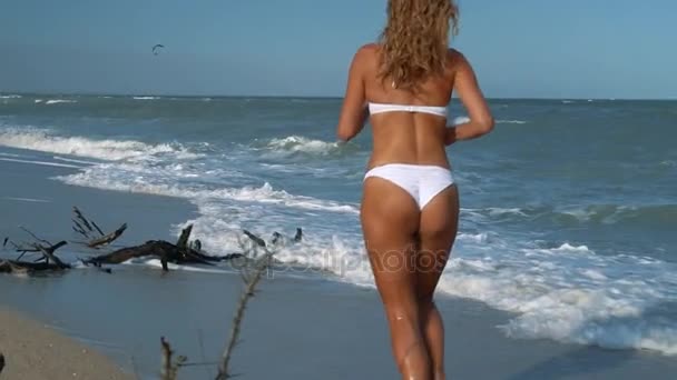 水着の若い美しいセクシーな日焼けした女の子は、ビーチに沿って走る。スローモーション。ステディカム. — ストック動画