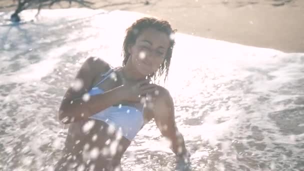 젊은 아름 다운 섹시 한 빠져 있 었 단된 소녀 비키니 바다에서 일몰 해변에 앉아 곱슬 머리에. 그녀는 enigmatically 미소, 자신에 게 그리고 슬로우 모션을 쓰다. 120 fps — 비디오