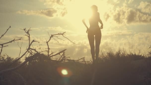 Jonge mooie sexy gelooid meisje in bikini met krullend haar dansen op het strand bij zonsondergang aan zee. Ze glimlachte raadselachtig, streelde zichzelf en Slow-motion. 120fps — Stockvideo