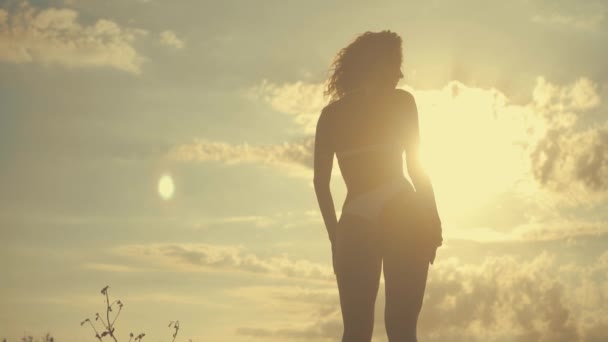 Ung vacker sexig garvade flicka i bikini med lockigt hår som dansar på stranden i solnedgången vid havet. Hon log gåtfullt, linjerade själv och slowmotion. 120fps — Stockvideo