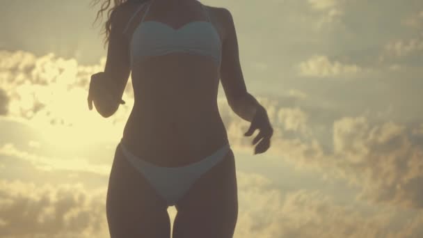 Ung vacker sexig garvade flicka i bikini med lockigt hår som dansar på stranden i solnedgången vid havet. Hon log gåtfullt, linjerade själv och slowmotion. 120fps — Stockvideo