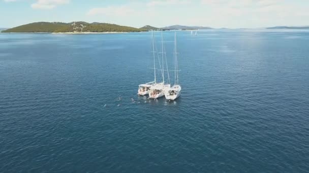 Vista aérea de tres yates de vela están conectados, cerca de hermosas islas. Hermosas nubes en el fondo. Yates de lujo en el mar. La gente nada cerca de yates — Vídeo de stock