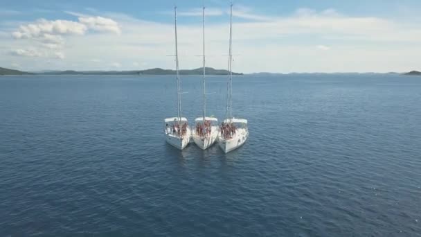 Vista aérea de tres yates de vela están conectados, cerca de hermosas islas. Hermosas nubes en el fondo. Yates de lujo en el mar. La gente nada cerca de yates — Vídeos de Stock