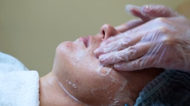 Женщина-косметолог делает косметическую маску для женщины-клиента в косметологическом центре. Очистка лица — стоковое видео