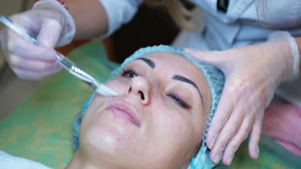 Женщина-косметолог делает косметическую маску для женщины-клиента в косметологическом центре. Очистка лица — стоковое видео