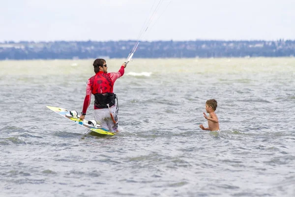 Vader en zoon zijn Kitesurfen aan de zee. De zoon klampt zich vast aan Papas terug — Stockfoto