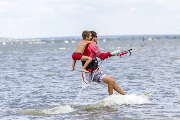 Tata i syn są kitesurfingu nad morzem. Syn przylega do Papas powrót — Zdjęcie stockowe