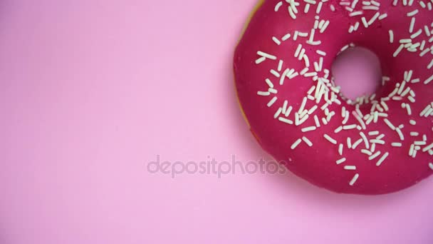 Deliciosa rosquilla dulce girando en un plato. Vista superior. Brillante y colorido espolvoreado donut primer plano macro disparo girando sobre un fondo rosa . — Vídeo de stock