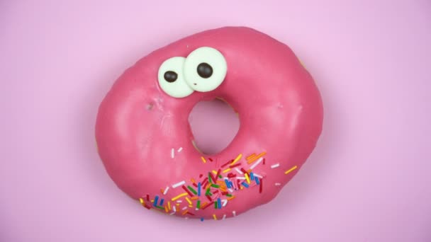 Delicious sweet donut rotating on a plate. Top view. Bright and colorful sprinkled donut close-up macro shot spinning on a pink background. — Stock Video