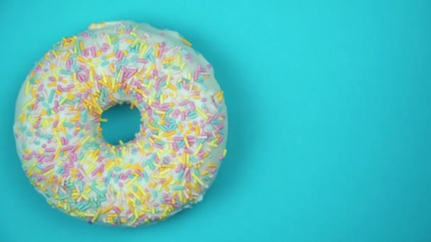 Delicioso donut doce girando em um prato. Vista superior. Brilhante e colorido donut polvilhado close-up macro tiro girando em um fundo azul . — Vídeo de Stock