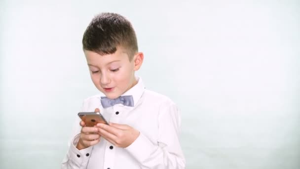 Menino mostra polegares para cima e brincando com um tablet ou smartphone no fundo branco — Vídeo de Stock