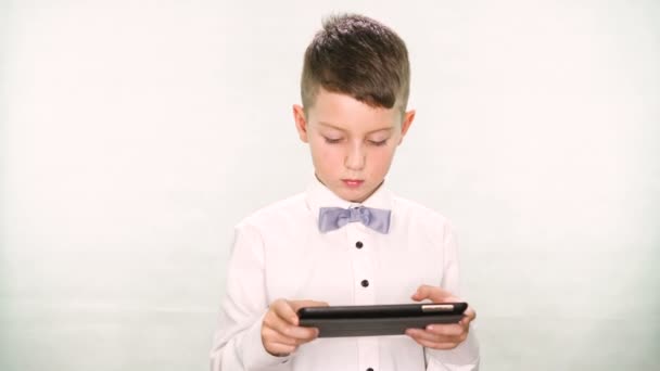 Niño muestra los pulgares hacia arriba y jugar con una tableta o teléfono inteligente sobre fondo blanco — Vídeos de Stock