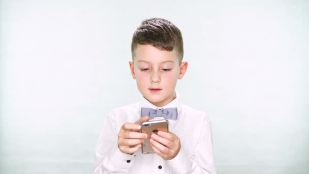 Niño muestra los pulgares hacia abajo y jugar con una tableta o teléfono inteligente sobre fondo blanco — Vídeos de Stock