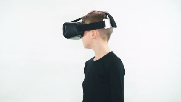 Маленький хлопчик у гарнітурі віртуальної реальності стоїть у білій кімнаті і дивиться навколо з подивом, десять намагається доторкнутися до чогось невидимого — стокове відео