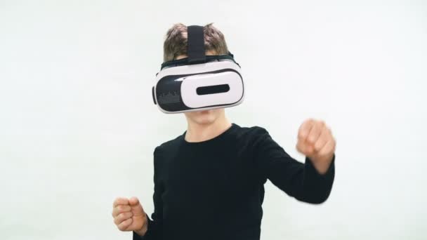 Маленький мальчик в наушниках виртуальной реальности, стоящий в белой комнате и оглядывающийся в изумлении, десять пытается прикоснуться к чему-то невидимому — стоковое видео