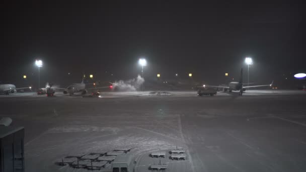 Una tormenta de nieve en el aeropuerto. Trabajadores y coches de servicio trabajan cerca de aviones — Vídeos de Stock