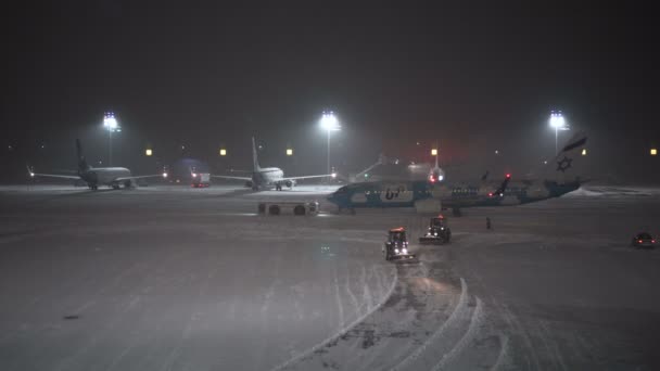 Una tormenta de nieve en el aeropuerto. Trabajadores y coches de servicio trabajan cerca de aviones — Vídeos de Stock