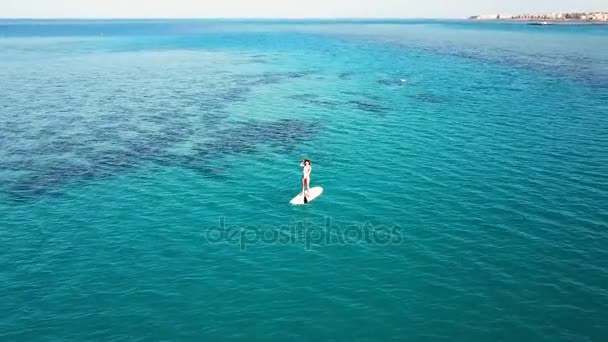 Vista aérea de chica joven de pie remando en vacaciones. Tracking shot of a young woman SUP boarding — Vídeos de Stock