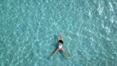Havadan görünümü. Güzel genç kadın beyaz bikini berrak Turkuaz rengi okyanus su yüzeyinde yüzen