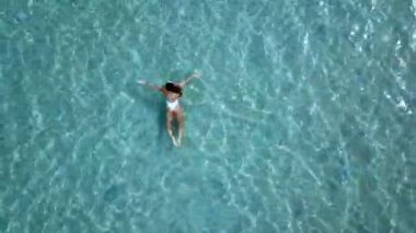 Havadan görünümü. Güzel genç kadın beyaz bikini berrak Turkuaz rengi okyanus su yüzeyinde yüzen