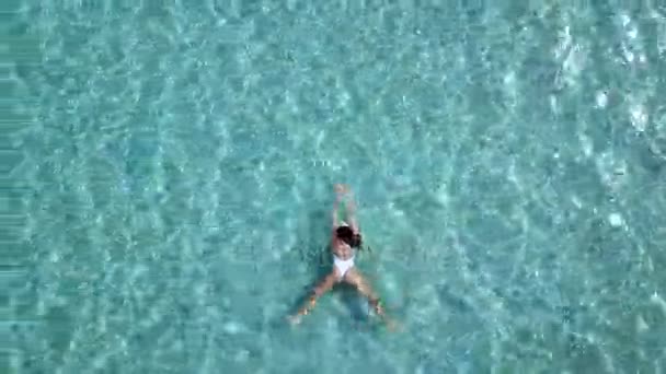 Vista aérea. Hermosa mujer joven en bikini blanco flotando en la superficie del agua en color turquesa cristalino océano — Vídeo de stock