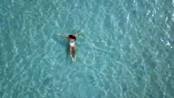 공중 볼 수 있습니다. 흰색 비키니 맑은 청록색 색 바다에서 물 표면에 떠 있는 아름 다운 젊은 여자 — 비디오