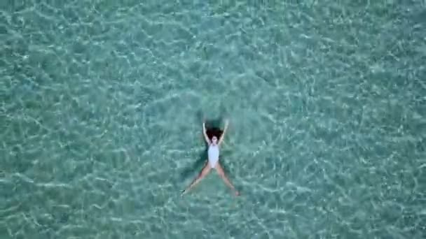 空撮。透き通ったターコイズ色の海の水面に浮かぶ白いビキニの美しい若い女性 — ストック動画