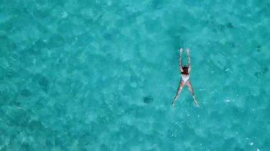 Havadan görünümü. Güzel genç kadın beyaz bikini berrak Turkuaz rengi okyanus su yüzeyinde yüzen