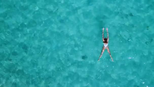 Aerial view. Beautiful young woman in white bikini floating on water surface in crystal clear turquoise color ocean — Stock Video