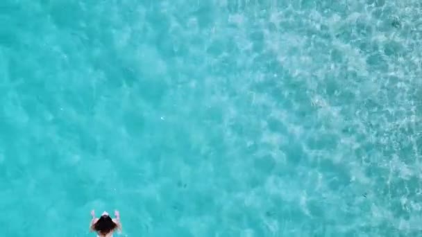 Vista aérea. Mulher bonita em biquíni branco flutuando na superfície da água no oceano de cor azul-turquesa cristalina — Vídeo de Stock