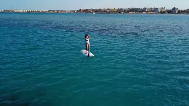 Vista aérea de chica joven de pie remando en vacaciones. Tracking shot of a young woman SUP boarding — Vídeo de stock