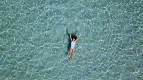 Luchtfoto. Mooie jonge vrouw in witte bikini drijvend op het wateroppervlak in turkoois kristalheldere Oceaan — Stockvideo