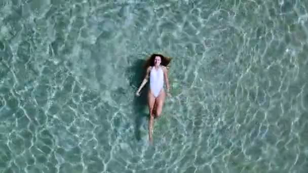 Vista aerea. Bella giovane donna in bikini bianco galleggiante sulla superficie dell'acqua in cristallino colore turchese oceano — Video Stock