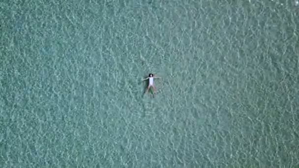 Luchtfoto. Mooie jonge vrouw in witte bikini drijvend op het wateroppervlak in turkoois kristalheldere Oceaan — Stockvideo