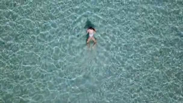 Aerial view. Beautiful young woman in white bikini floating on water surface in crystal clear turquoise color ocean — Stock Video