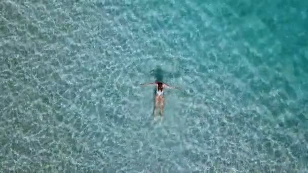 Aerial view. Beautiful young woman in white bikini floating on water surface in crystal clear turquoise color ocean — Stock Video