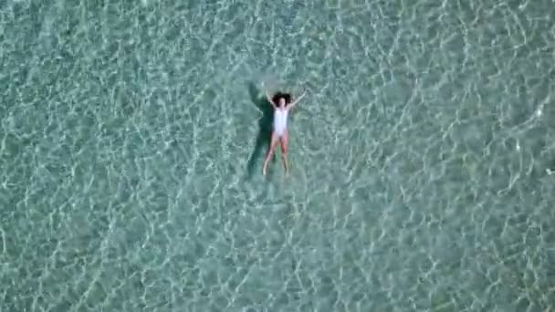 Вид з повітря. Красива молода жінка в білому бікіні плаває на поверхні води в кришталево чистому бірюзовому кольорі океану — стокове відео
