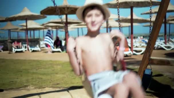 Мальчик качается на качелях на детской площадке . — стоковое видео