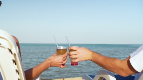 Young family couple sunbathing and drinking colored cocktail at tropical beach. Lovers on honeymoon have exotic vacation lying in the sun on deck chairs near ocean — Stock Video