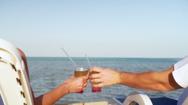 Jovem casal familiar tomando sol e bebendo coquetel colorido na praia tropical. Os amantes na lua de mel têm férias exóticas deitadas ao sol em cadeiras de convés perto do oceano — Vídeo de Stock