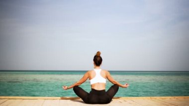 Kızı ada sahilde poz yoga yapıyor. Statik. Deniz ya da okyanus mutlu kadın gevşeme. Su ve bulutlar. El ve mavi gökyüzü.